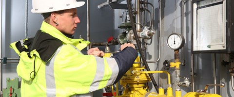 Junger Mitarbeiter in Warnschutzjacke und Helm arbeitet mit Schraubenschlüssel an einer Anlage Junger Mitarbeiter in Warnschutzjacke und Helm arbeitet mit Schraubenschlüssel an einer Anlage