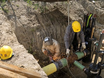 Zwei Mitarbeiter bei Schweißarbeiten an einem Rohr in einer Baugrube Zwei Mitarbeiter bei Schweißarbeiten an einem Rohr in einer Baugrube