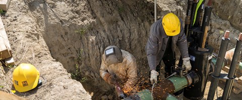 Zwei Mitarbeiter bei Schweißarbeiten an einem Rohr in einer Baugrube Zwei Mitarbeiter bei Schweißarbeiten an einem Rohr in einer Baugrube
