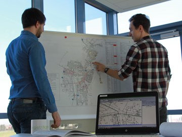 Zwei Männer in einem Büro vor einem Whiteboard mit Plänen Zwei Männer in einem Büro vor einem Whiteboard mit Plänen