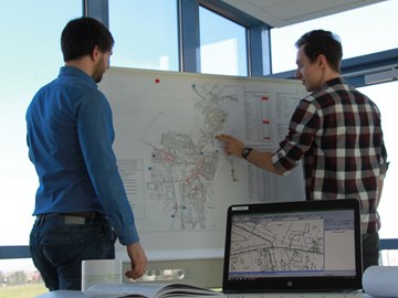 Zwei Männer in einem Büro vor einem Whiteboard mit Plänen Zwei Männer in einem Büro vor einem Whiteboard mit Plänen