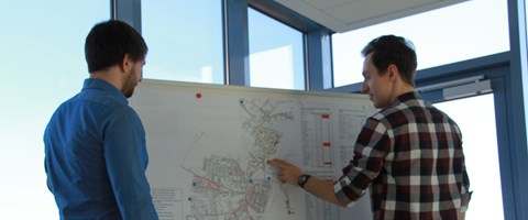 Zwei Männer in einem Büro vor einem Whiteboard mit Plänen Zwei Männer in einem Büro vor einem Whiteboard mit Plänen