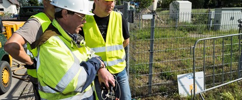 Drei Mitarbeiter mit Warnwesten und Helmen am Zaun einer Baustelle Drei Mitarbeiter mit Warnwesten und Helmen am Zaun einer Baustelle