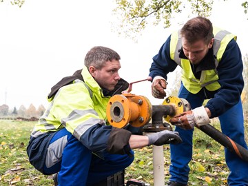 Zwei Mitarbeiter arbeiten an einer Leitung auf einem Feld Zwei Mitarbeiter arbeiten an einer Leitung auf einem Feld