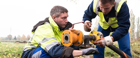 Zwei Mitarbeiter arbeiten an einer Leitung auf einem Feld Zwei Mitarbeiter arbeiten an einer Leitung auf einem Feld