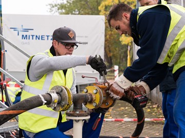 Zwei Mitarbeiter arbeiten mit Werkzeugen an einer Leitung auf einer Straße Zwei Mitarbeiter arbeiten mit Werkzeugen an einer Leitung auf einer Straße