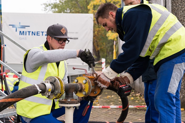 Zwei Mitarbeiter arbeiten mit Werkzeugen an einer Leitung auf einer Straße Zwei Mitarbeiter arbeiten mit Werkzeugen an einer Leitung auf einer Straße