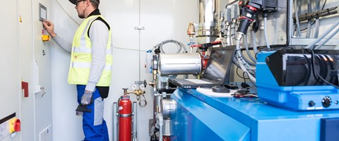 Mitarbeiter steht in einem Technikraum und bedient das Display einer Anlage Mitarbeiter steht in einem Technikraum und bedient das Display einer Anlage