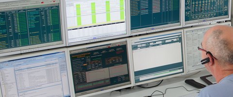 Mitarbeiter mit Headset sitzt an einem Tisch vor einer Tastatur und blickt auf acht Monitore Mitarbeiter mit Headset sitzt an einem Tisch vor einer Tastatur und blickt auf acht Monitore