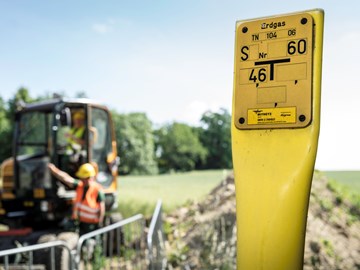 Erdgas-Schieber auf einem Feld, im Hintergrund Arbeiter mit einem Bagger Erdgas-Schieber auf einem Feld, im Hintergrund Arbeiter mit einem Bagger