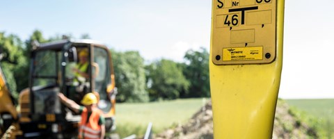 Erdgas-Schieber auf einem Feld, im Hintergrund Arbeiter mit einem Bagger Erdgas-Schieber auf einem Feld, im Hintergrund Arbeiter mit einem Bagger