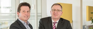 Dr. Schweer und Herr Hiersig an einem Counter über Unterlagen - blicken in die Kamera Dr. Schweer und Herr Hiersig an einem Counter über Unterlagen - blicken in die Kamera