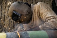 Mitarbeiter in schwerer Schutzkleidung schweißt ein Rohr Mitarbeiter in schwerer Schutzkleidung schweißt ein Rohr