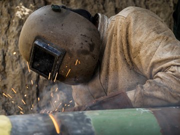 Mitarbeiter in schwerer Schutzkleidung schweißt ein Rohr Mitarbeiter in schwerer Schutzkleidung schweißt ein Rohr