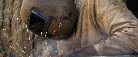 Mitarbeiter in schwerer Schutzkleidung schweißt ein Rohr Mitarbeiter in schwerer Schutzkleidung schweißt ein Rohr