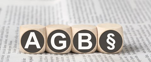 Vier Holzwürfel auf einer Zeitung zeigen die Abkürzung AGB und das Paragrafenzeichen Vier Holzwürfel auf einer Zeitung zeigen die Abkürzung AGB und das Paragrafenzeichen