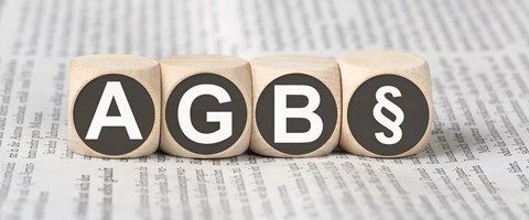 Vier Holzwürfel auf einer Zeitung zeigen die Abkürzung AGB und das Paragrafenzeichen Vier Holzwürfel auf einer Zeitung zeigen die Abkürzung AGB und das Paragrafenzeichen