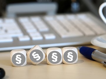 Vier Holzwürfel auf einem Schreibtisch neben einem Kugelschreiber vor einer Tastatur zeigen alle das Paragrafenzeichen Vier Holzwürfel auf einem Schreibtisch neben einem Kugelschreiber vor einer Tastatur zeigen alle das Paragrafenzeichen