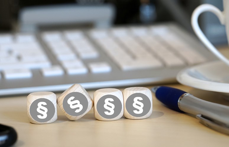 Vier Holzwürfel auf einem Schreibtisch neben einem Kugelschreiber vor einer Tastatur zeigen alle das Paragrafenzeichen Vier Holzwürfel auf einem Schreibtisch neben einem Kugelschreiber vor einer Tastatur zeigen alle das Paragrafenzeichen